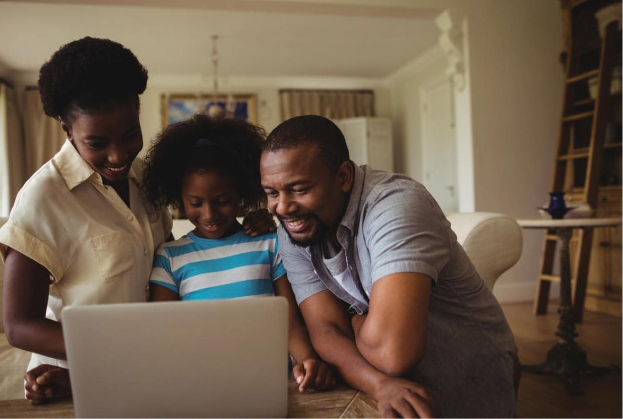 Child and her parents looking happily at a laptop screen