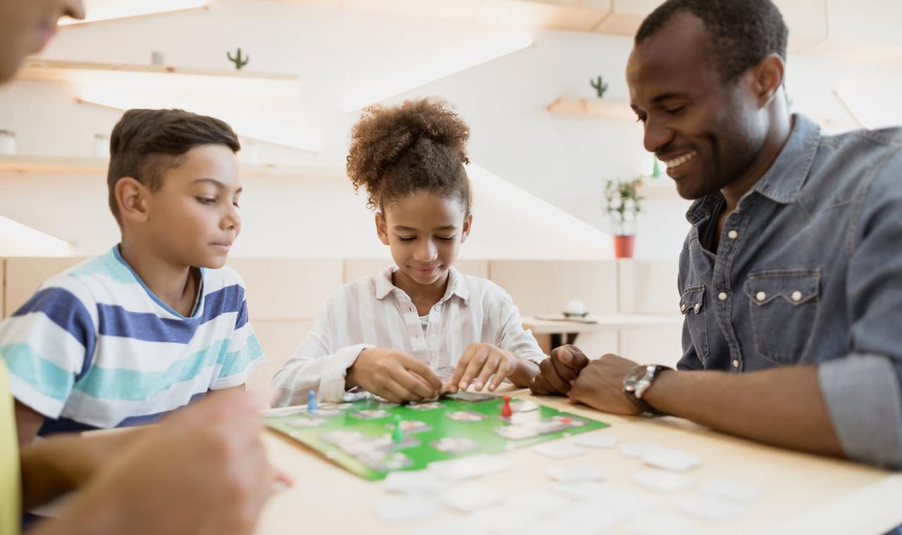 Father and two children sitting at a table and playing a board game together