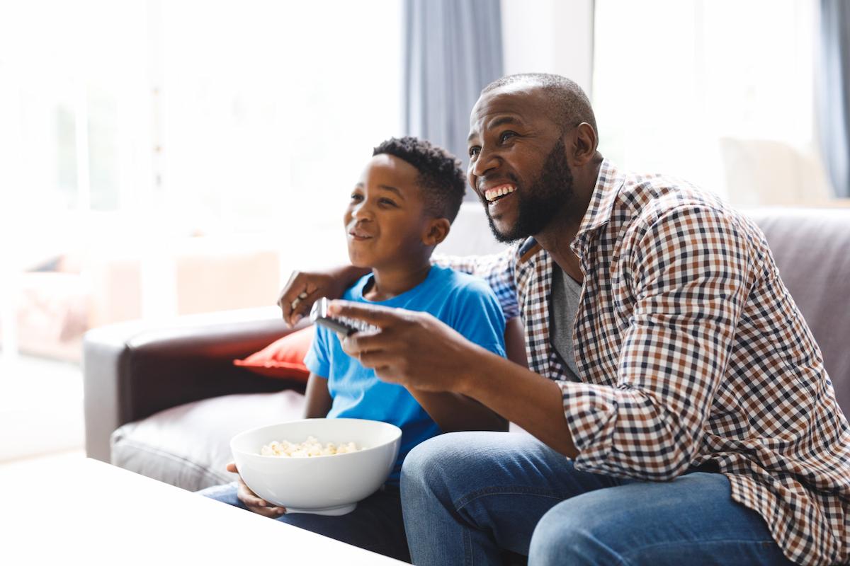 Father and son sitting on the sofa and watching TV together with popcorn