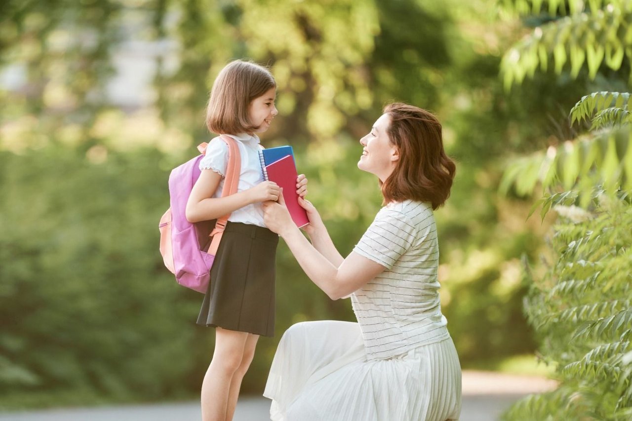 Happy schoolgirl taking books from her smiling mother in a bright, natural setting