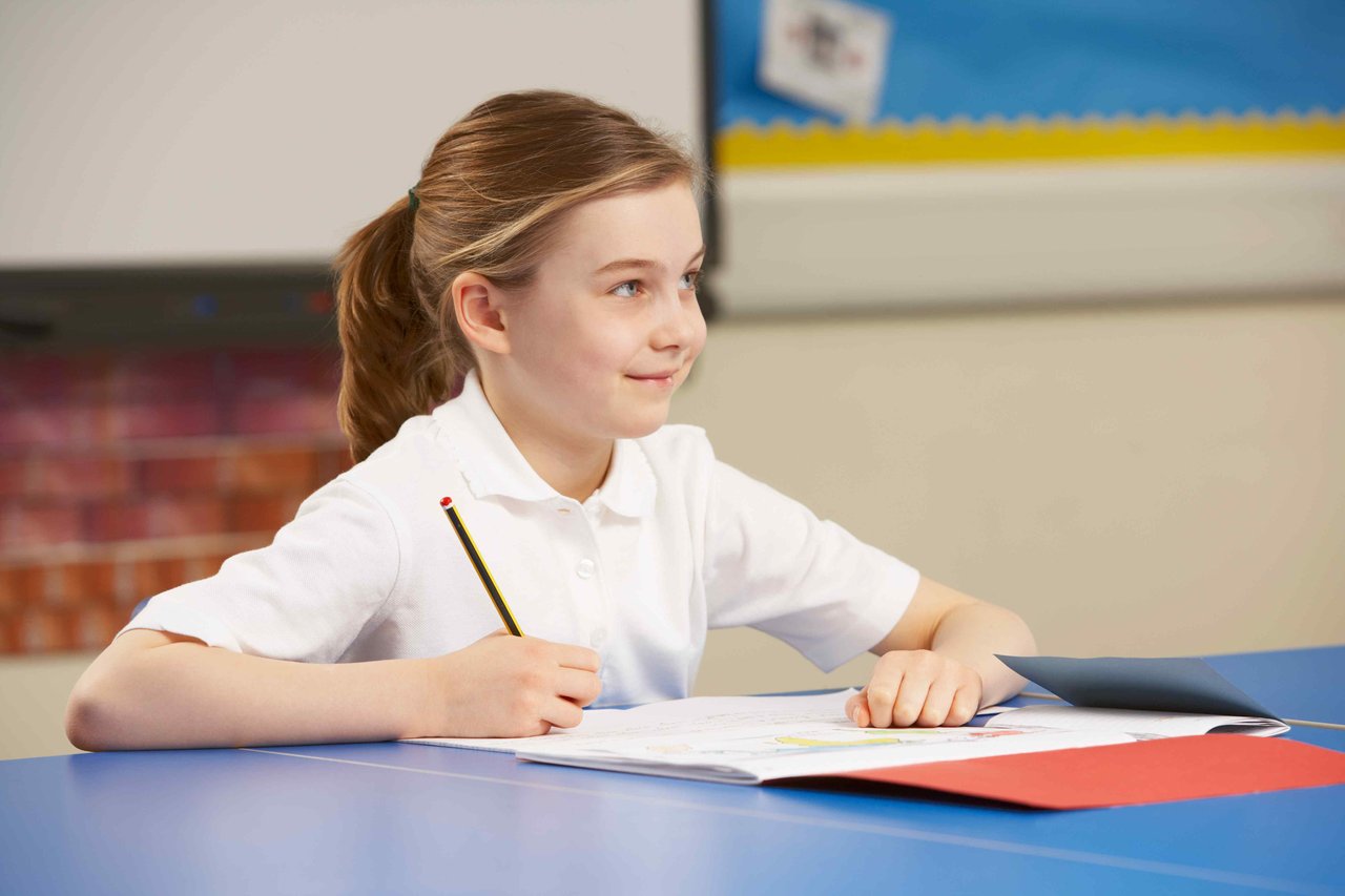 A young girl in school uniform sat in a primary school classroom working in a notebook