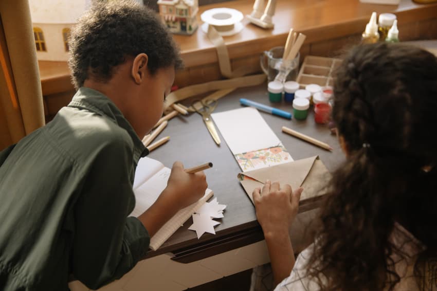 Two children sitting at a desk writing letters