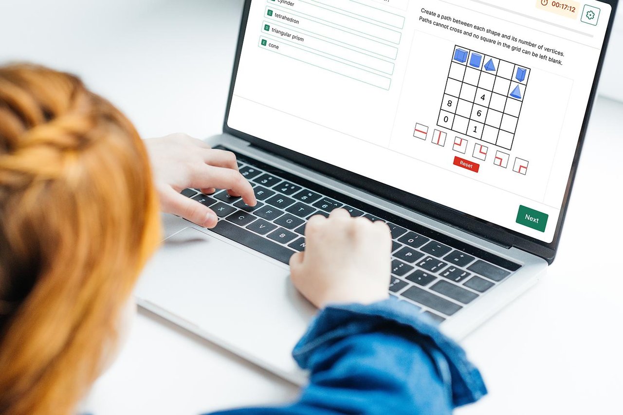 A child using a laptop in a bright modern room, showing a Quest Admissions puzzles and problem-solving question on the screen