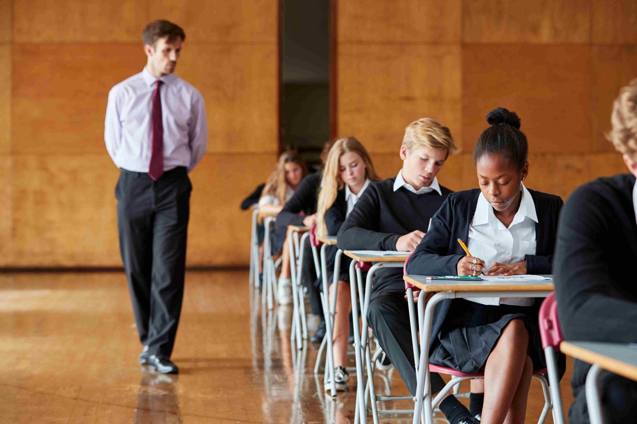 A group of Year 11 student sitting an exam in an exam hall with a teacher observing them