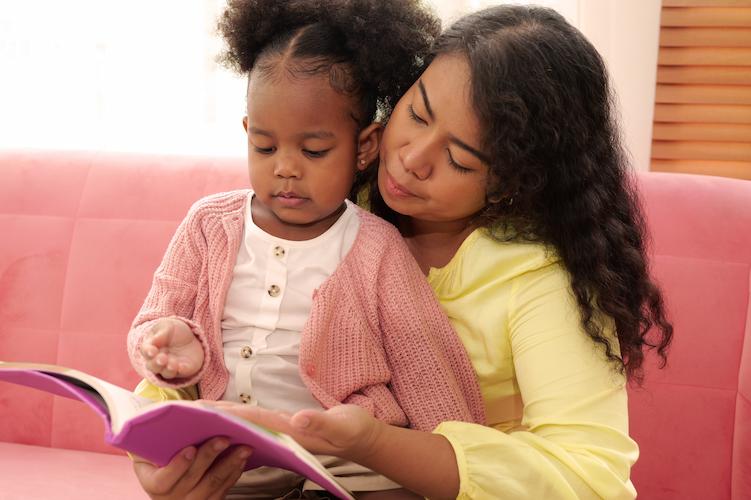 A parent and young child sat on their lap, reading the same book together