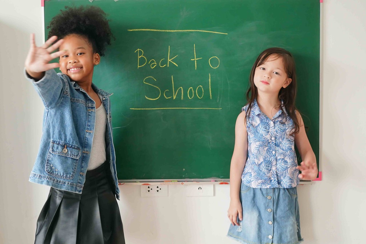 Two young girls stood in front of a chalk board with back to school written on it