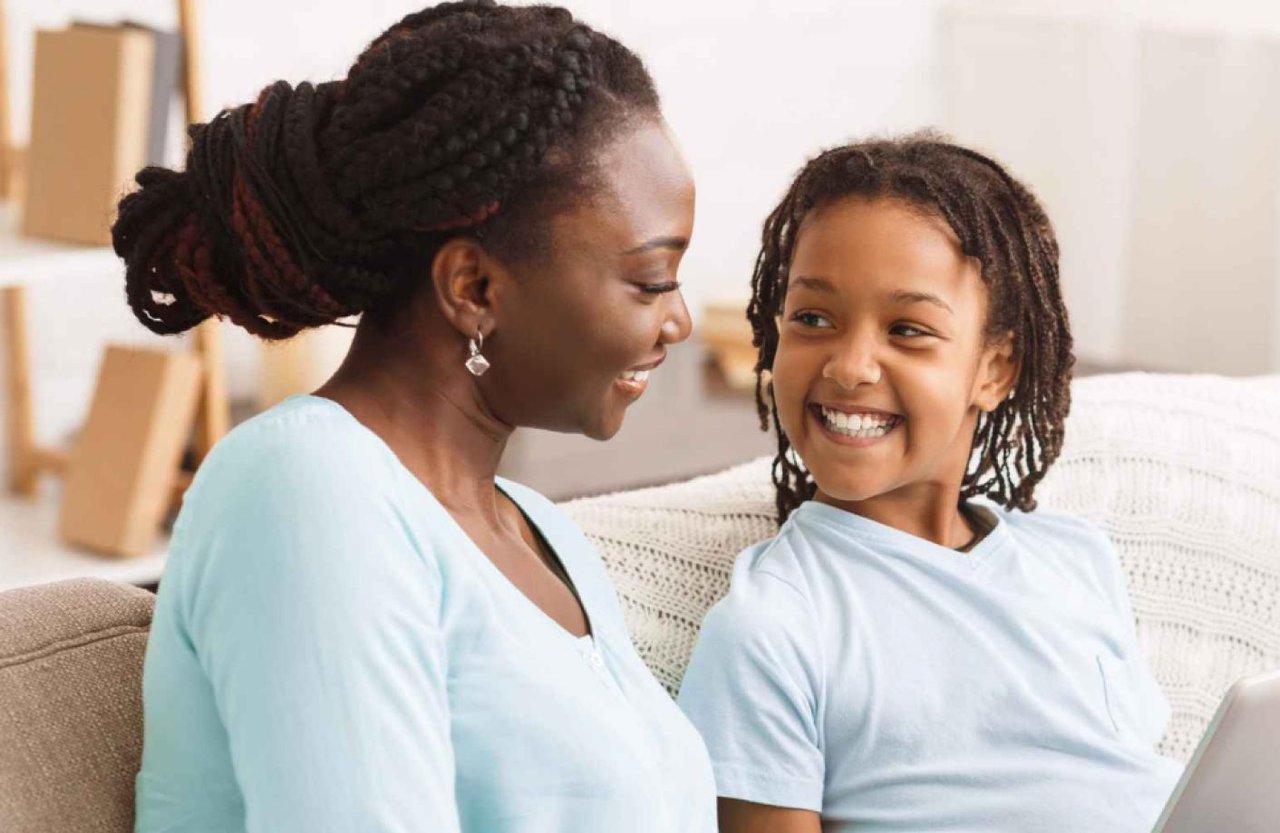 Young child and mother sitting on a sofa with a laptop and smiling at each other