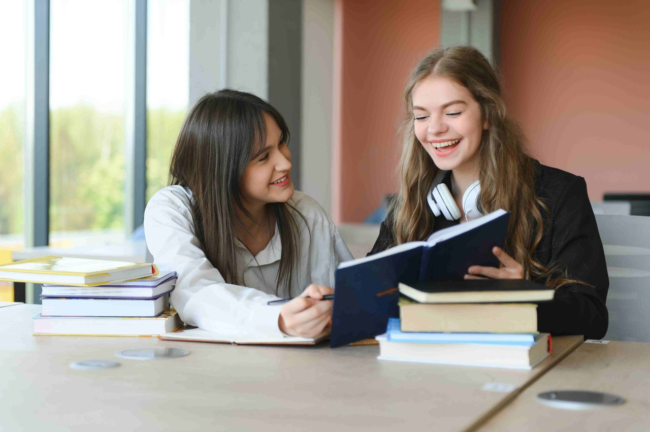 Two female students laughing whilst reading a book