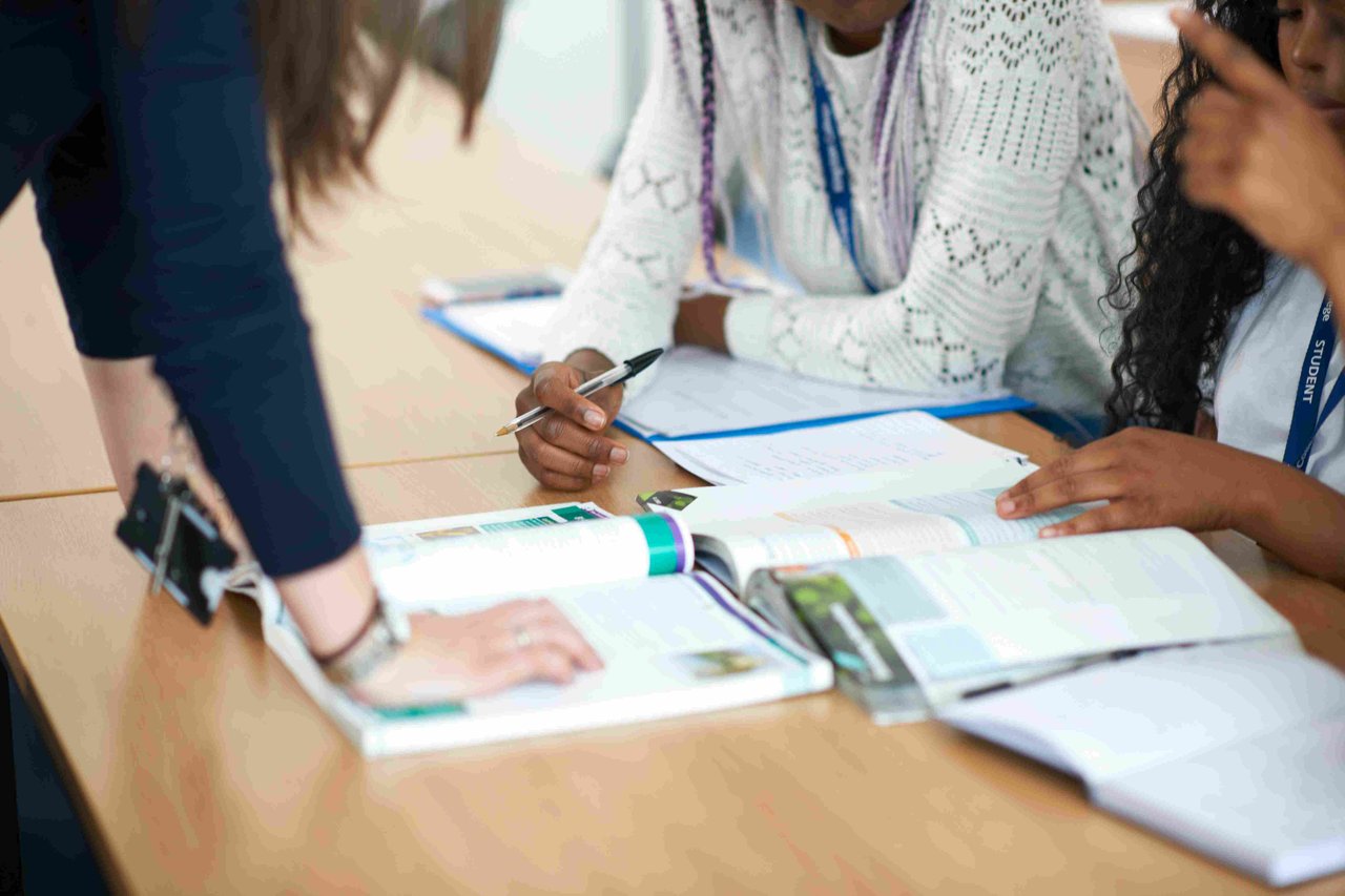 A teacher and group of students gathered around text books on a table