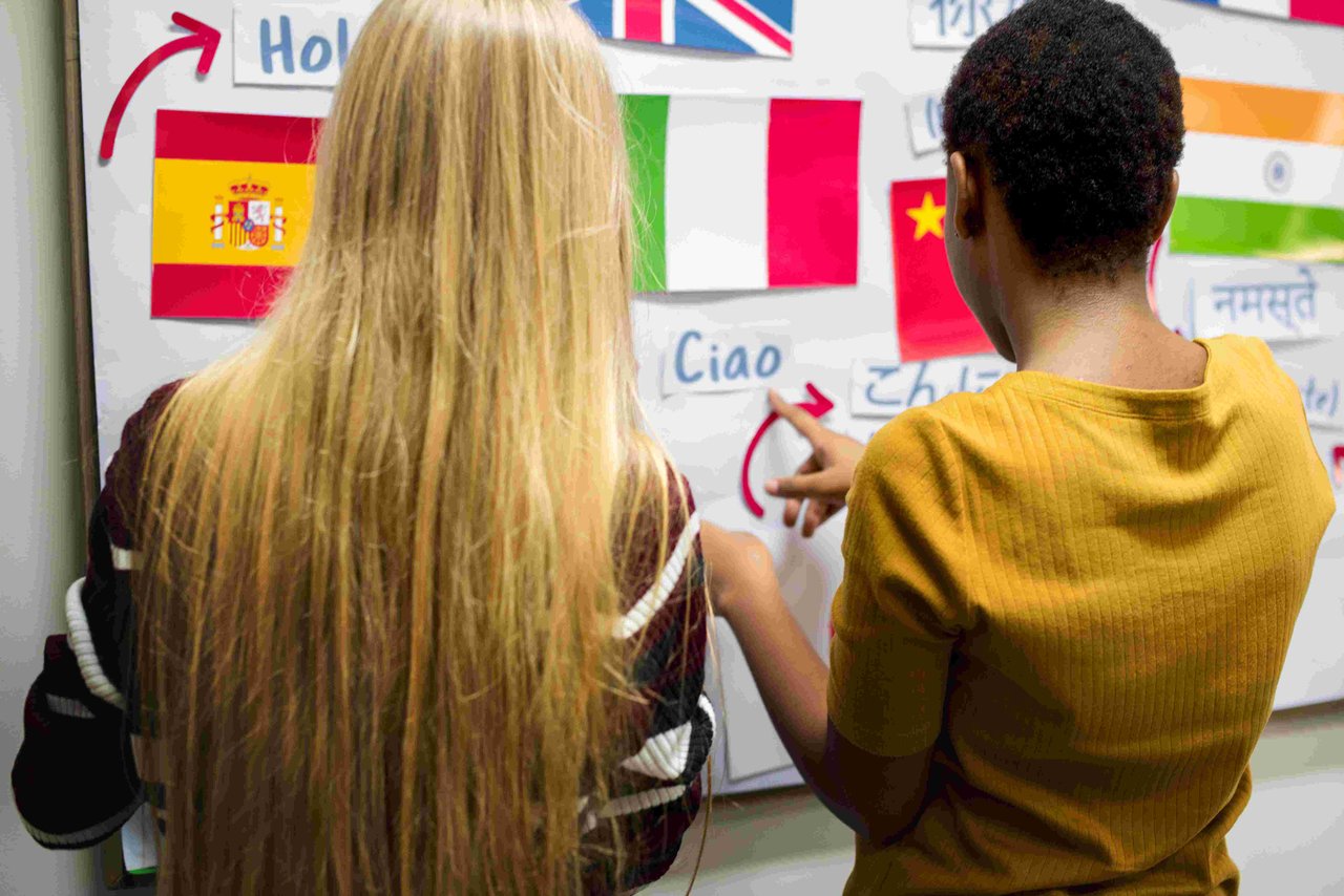 Two female GCSE student pointing at a whiteboard with lots of different phrases in different languages