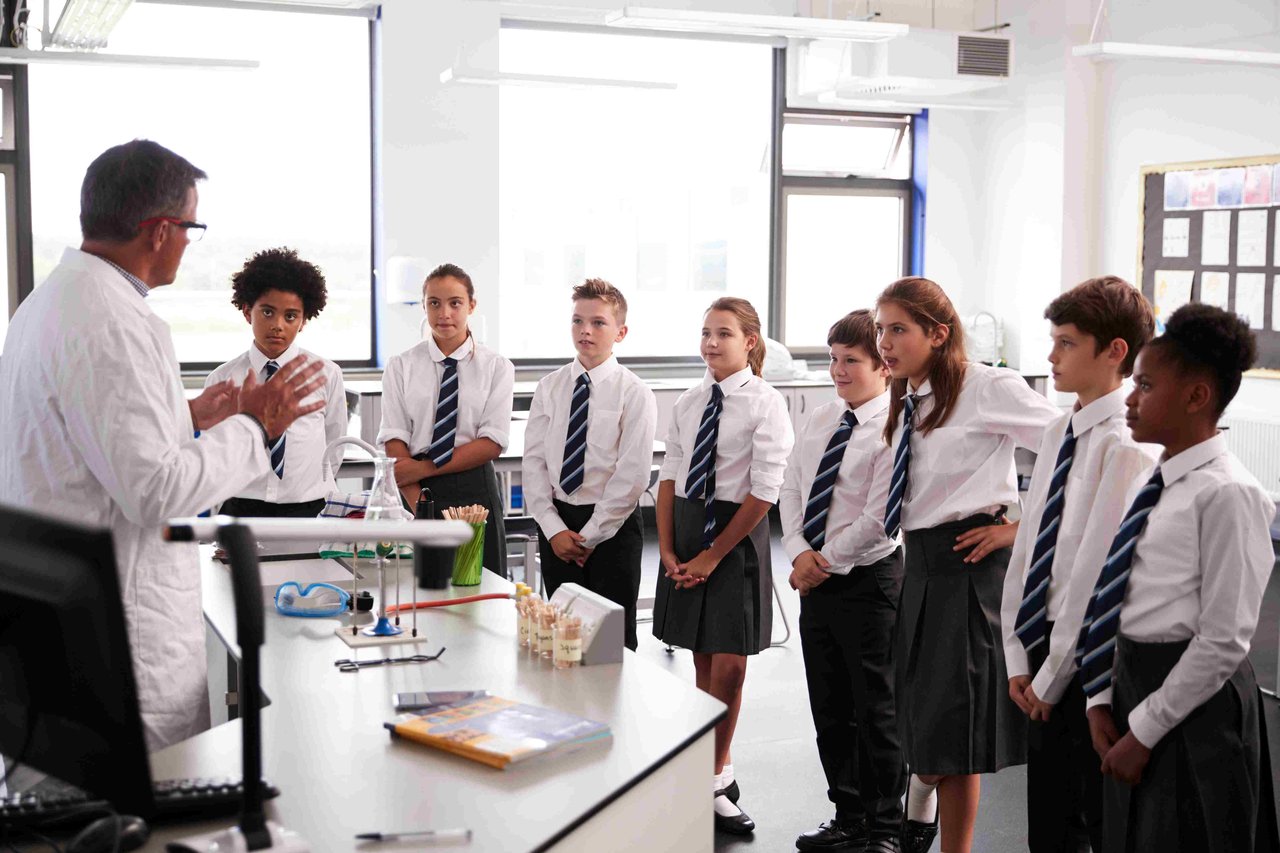 A group of secondary school students listening to a teacher in a science classroom