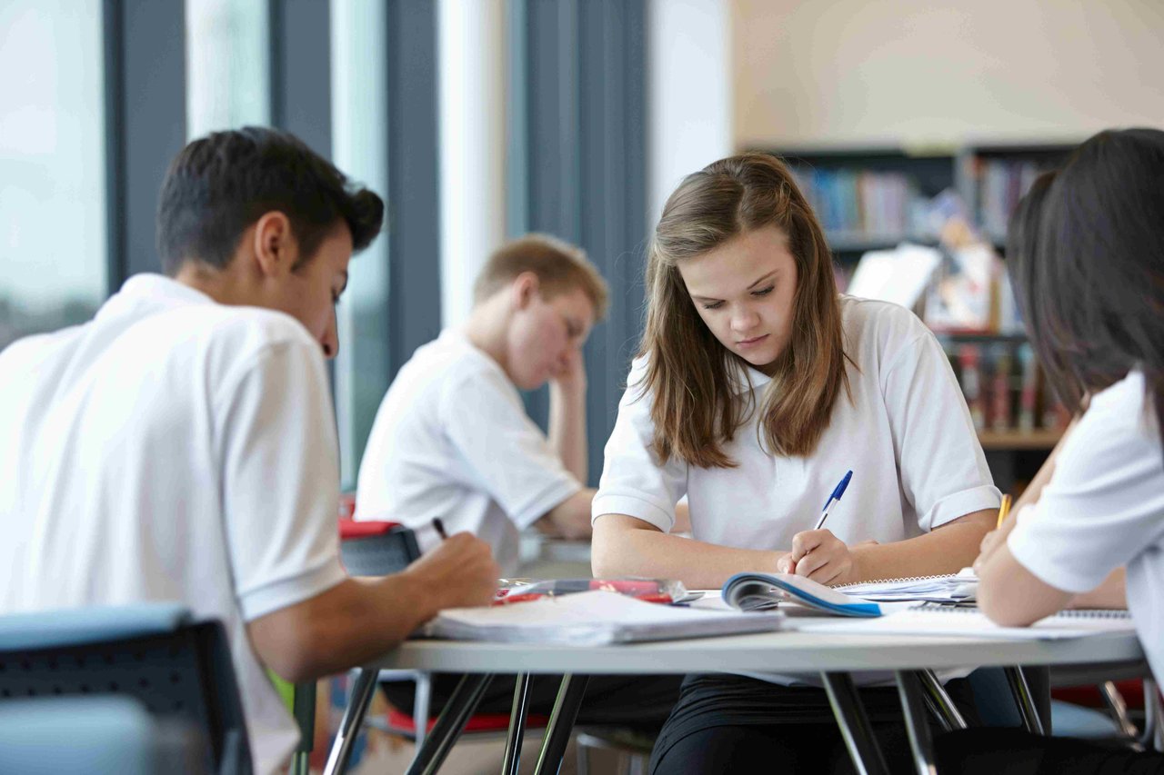 A group of GCSE studies sat around a table in a classroom writing