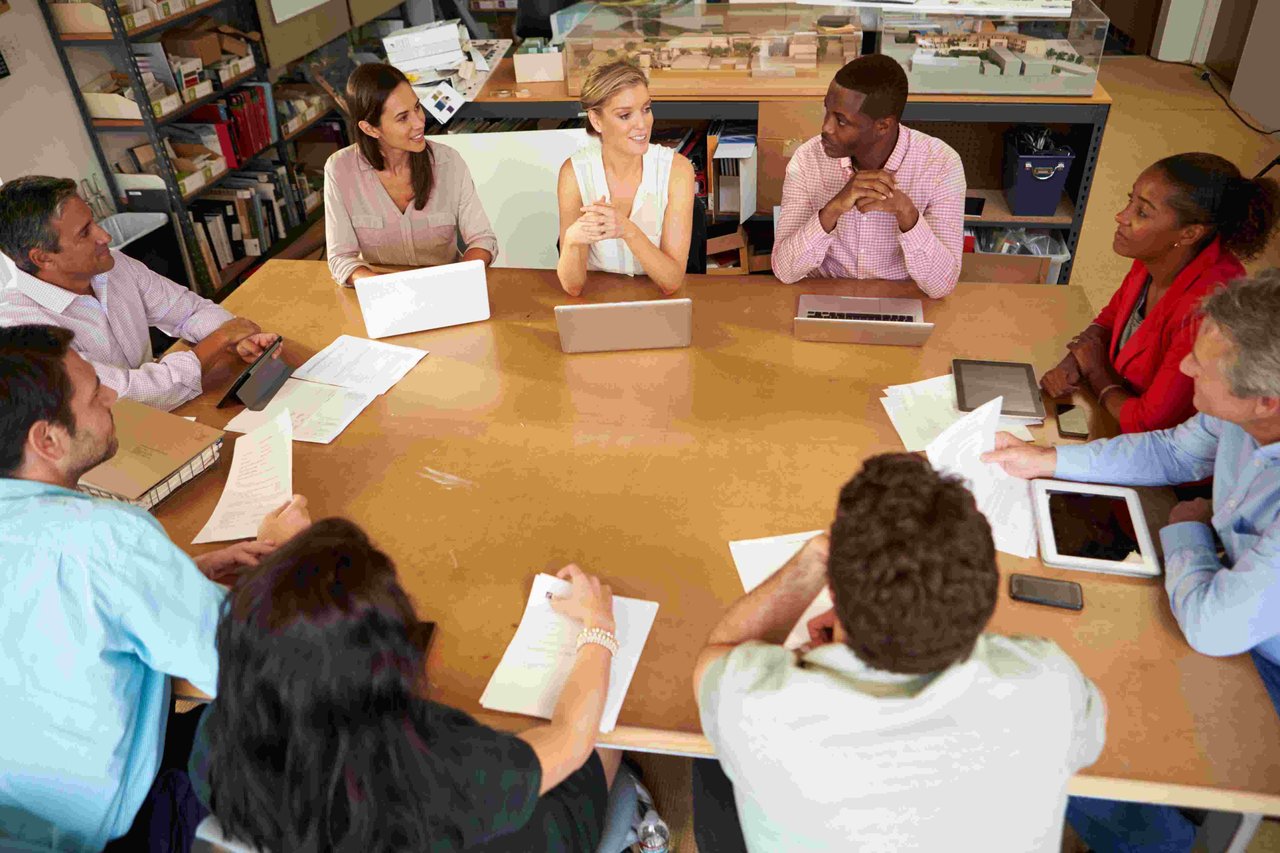 A group of teachers sat around a table with notebooks, laptops and tablets in front of them