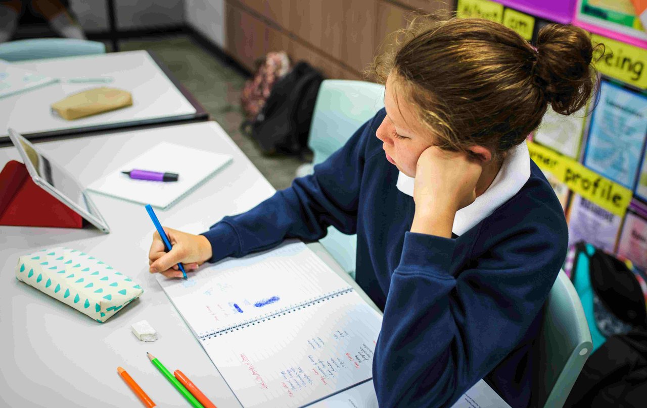 A female student, sat at a classroom desk writing in a notebook