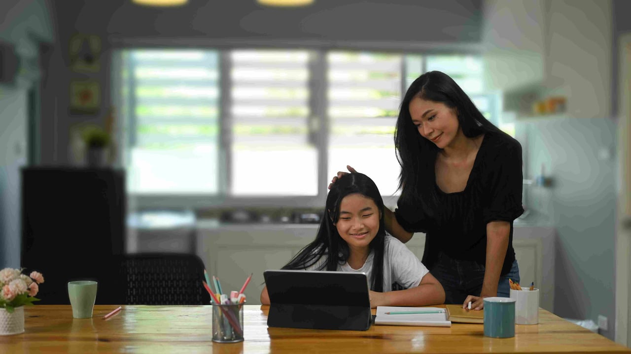A mother standing over her daughter looking at a laptop screen together