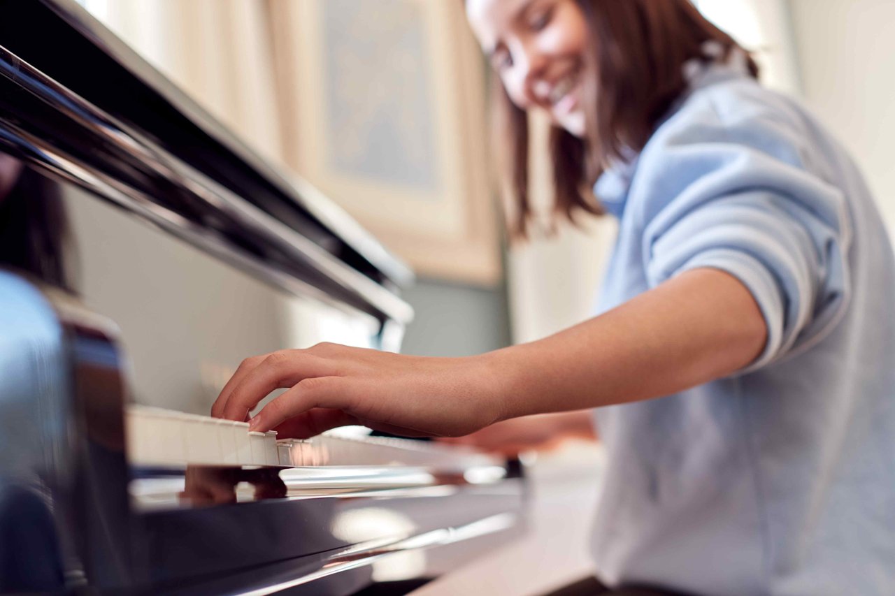 Schoolgirl in blue shirt smiling while playing the piano