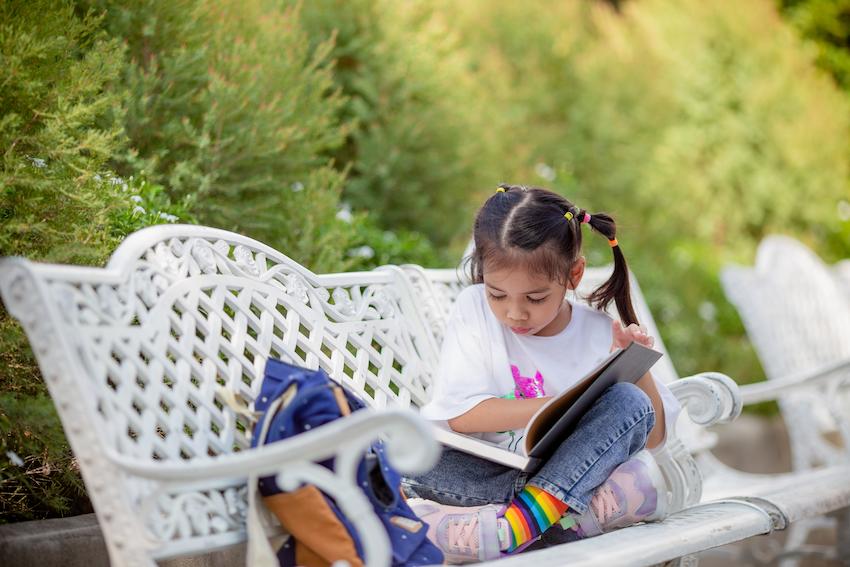 Young girl sat on a white bench reading a book