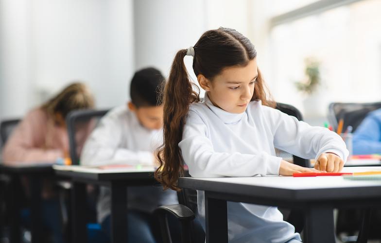 Portrait of small girl sitting at desk in classroom