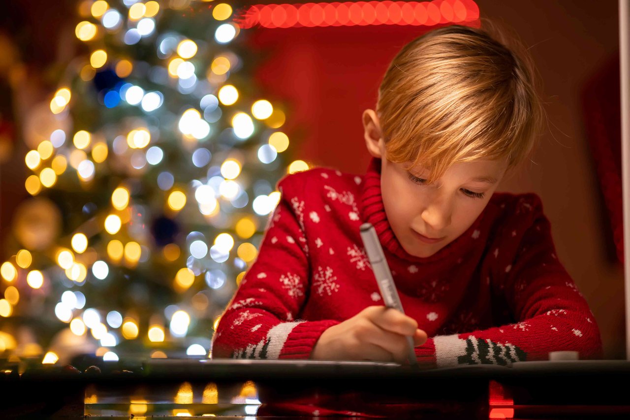 Boy in red Christmas jumper working at a table with christmas tree in background