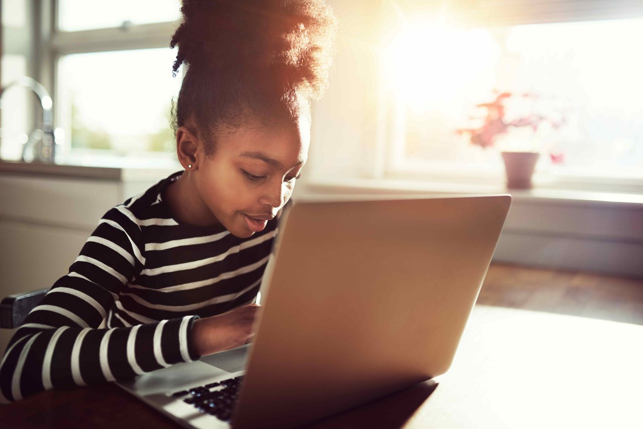 Young girl in a stripey black and white top sitting at the kitchen table in front of a laptop