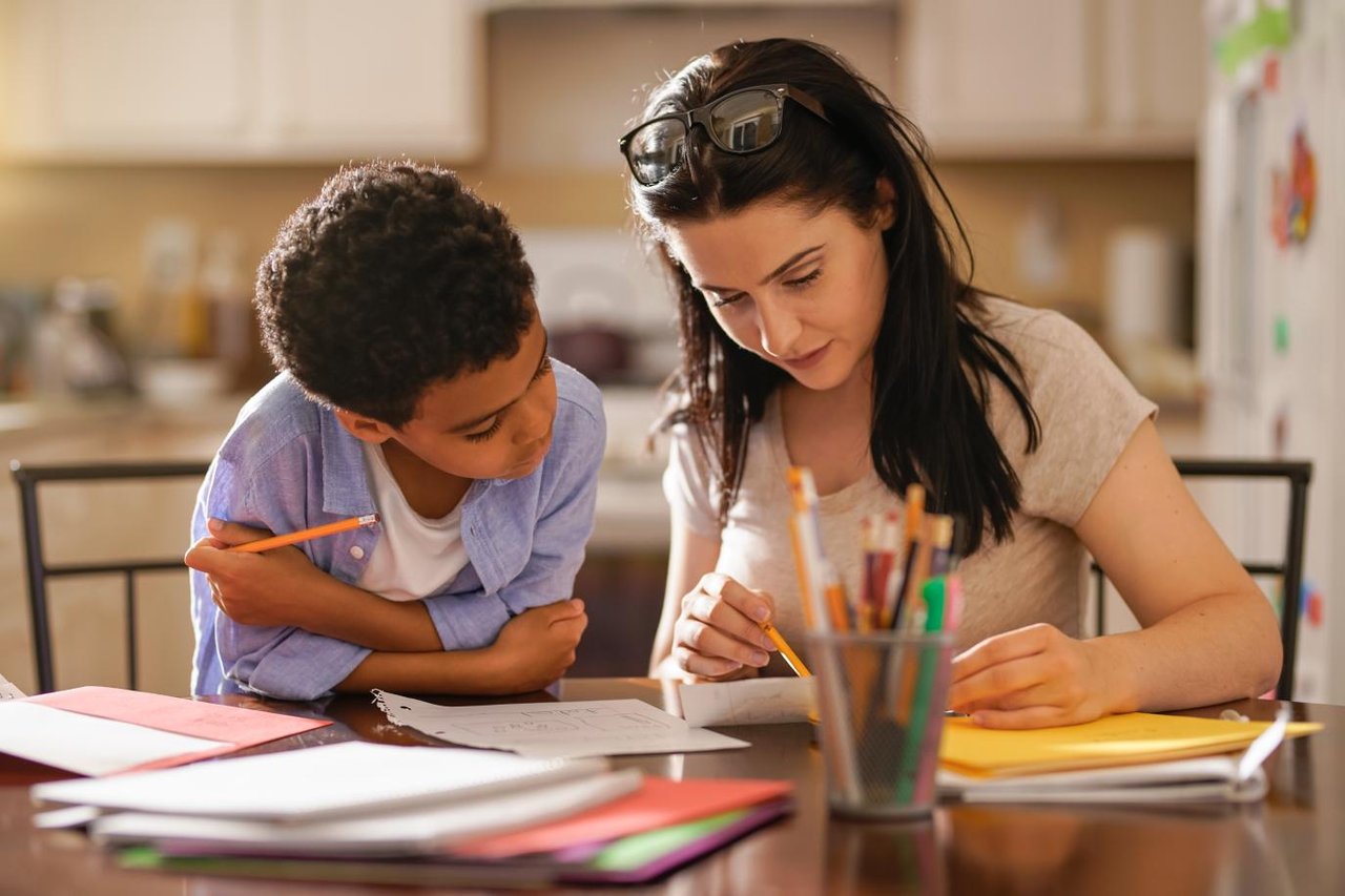 Mother and child sitting at a kitchen table. The mother is pointing something out to the child on a piece of paper. 