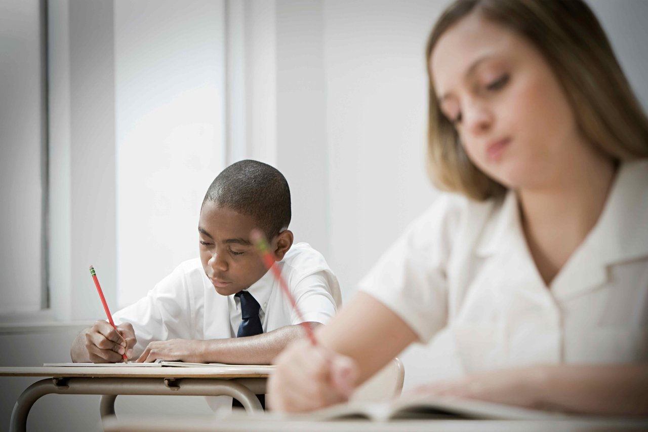 Boy and girl in school shirts taking a test in a brightly lit classroom