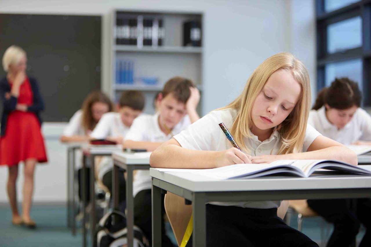 Female teacher watching children in a classroom doing an exam