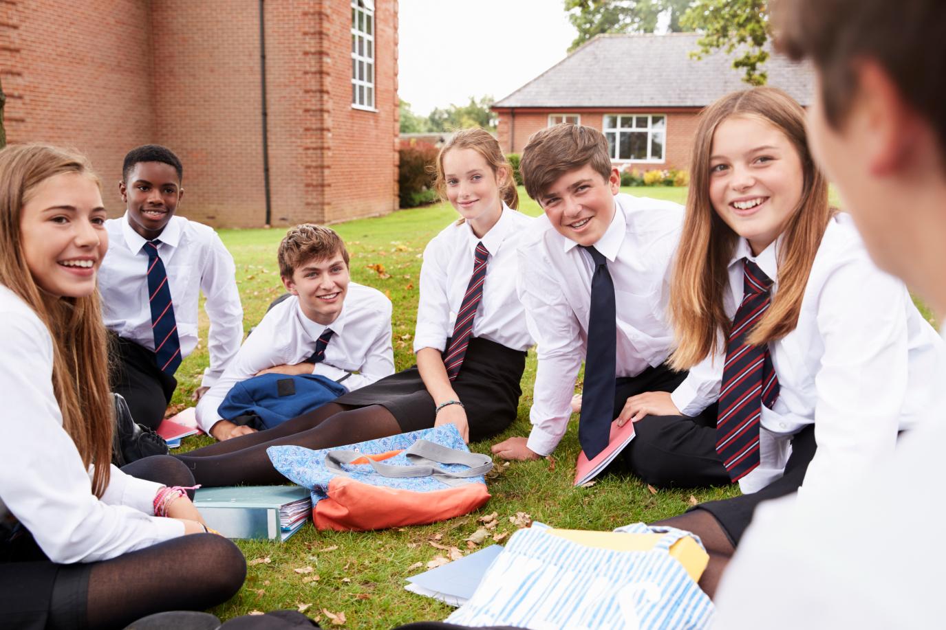 Group of teenagers in school uniform sitting and talking on the school grounds