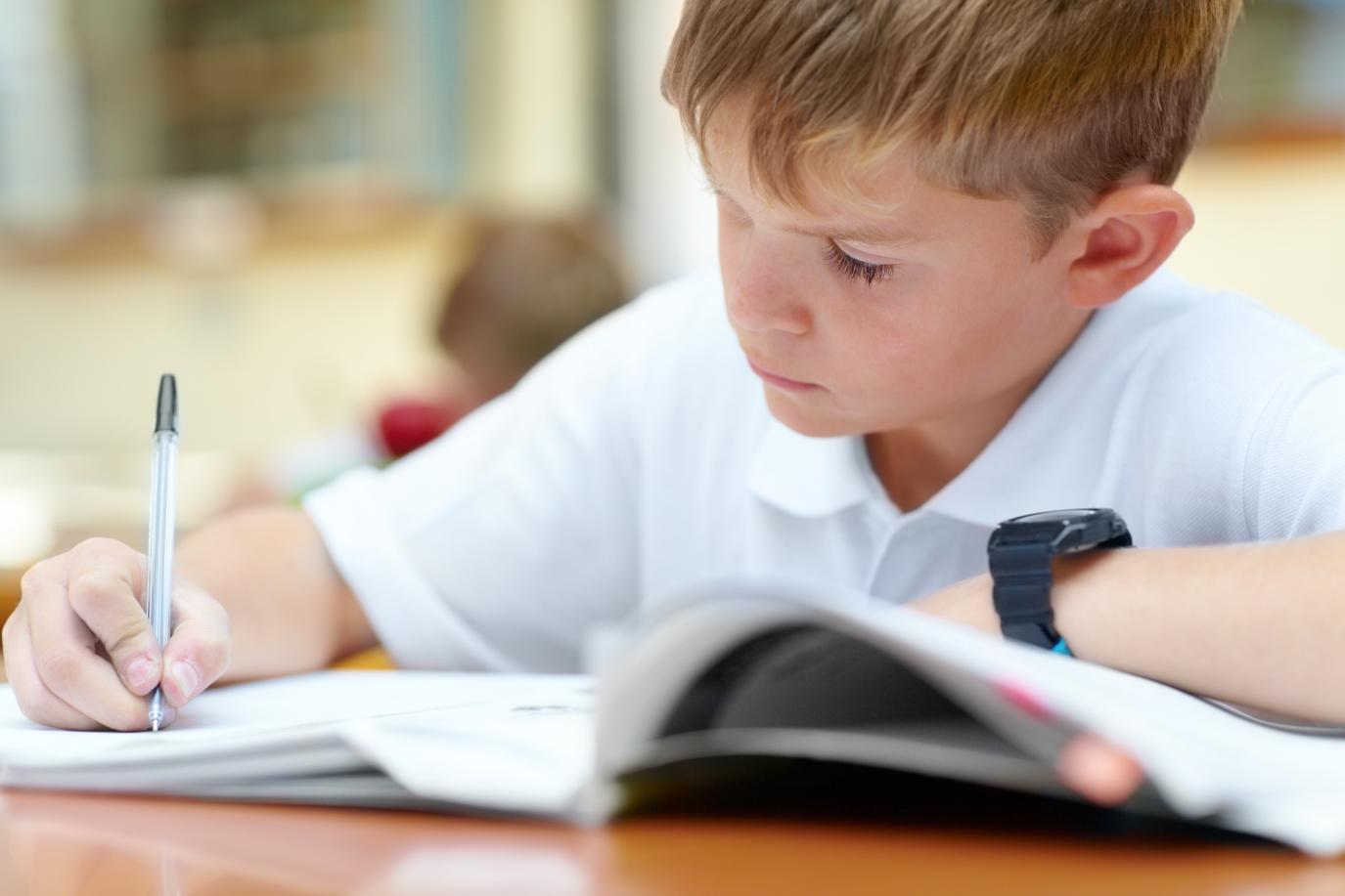 Boy wearing school uniform white polo concentrating while writing in an exercise book