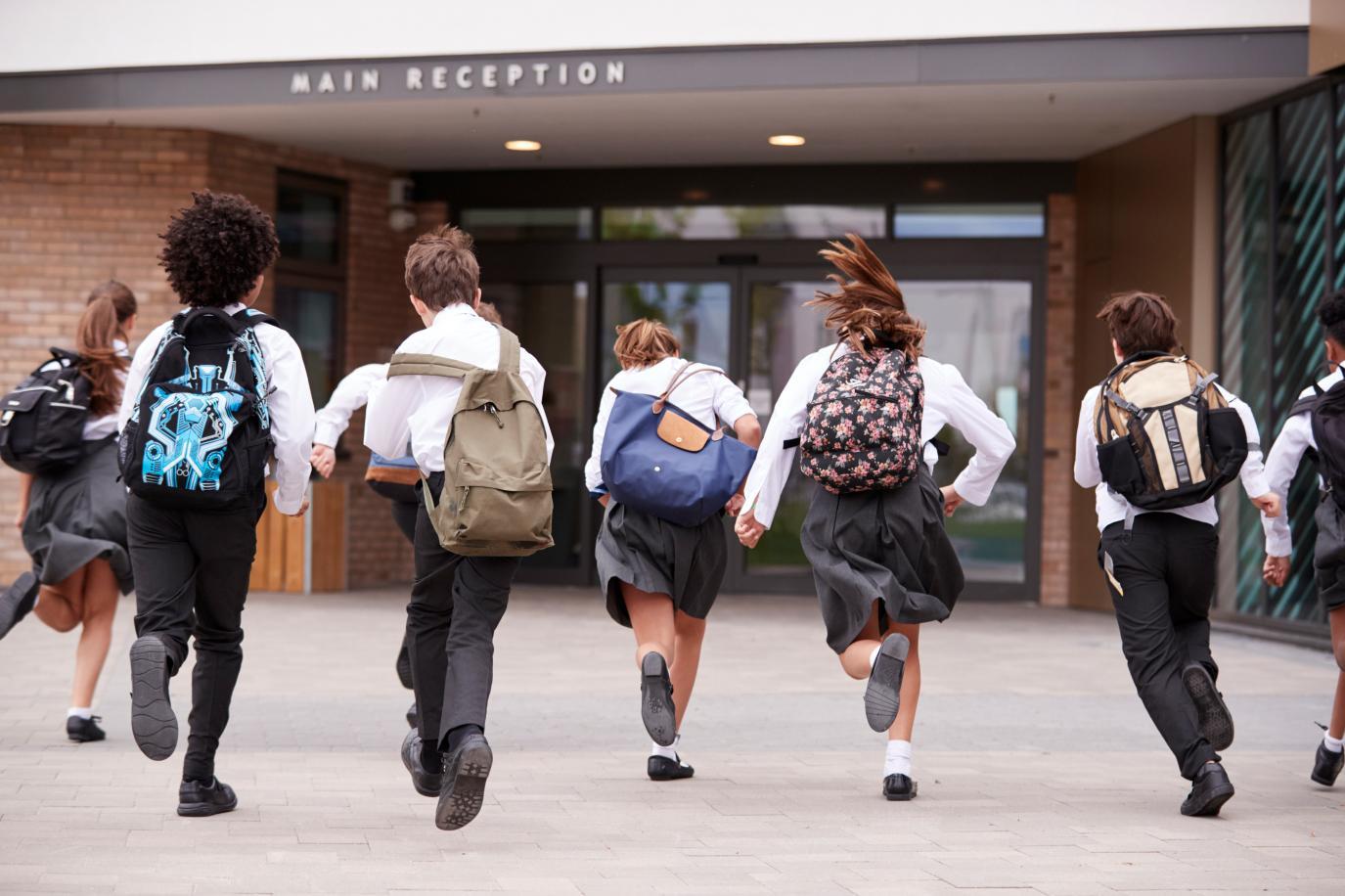 Children in school uniform and backpacks running towards a school building named 'Main Reception'