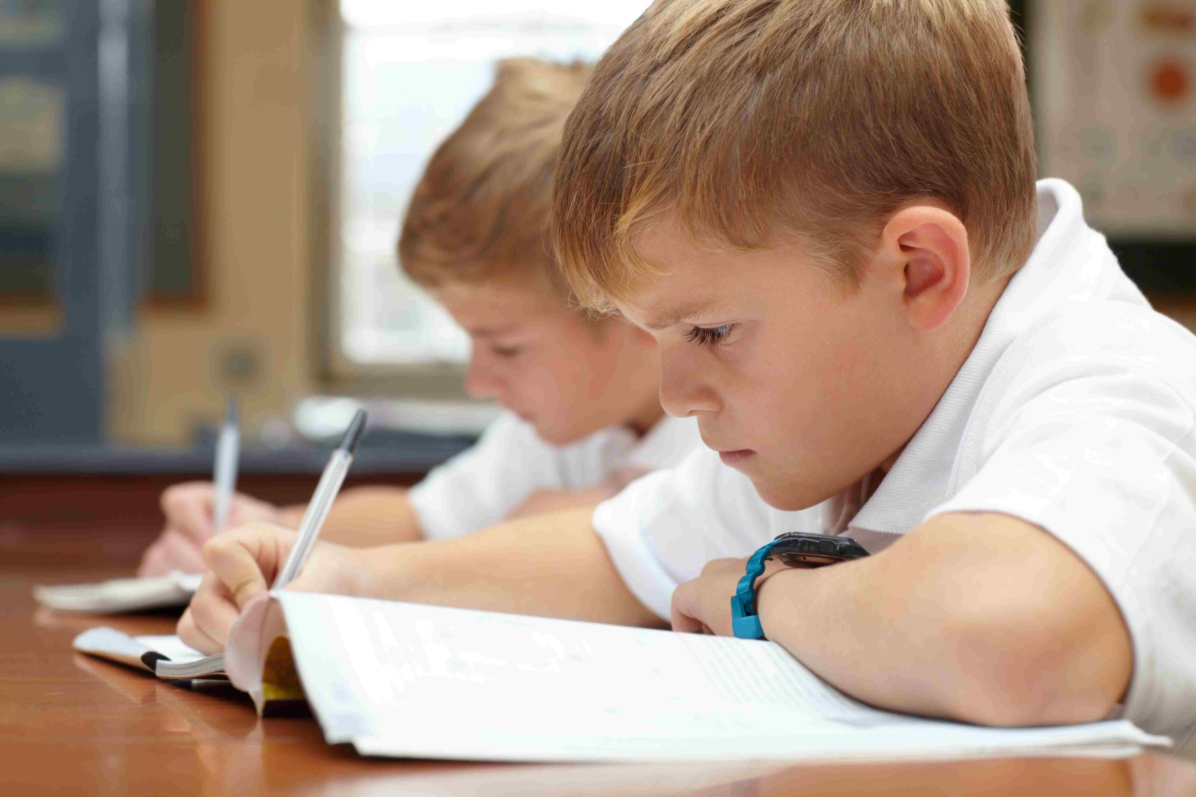 Two boys in white school polo shirts hard at work writing in test booklets