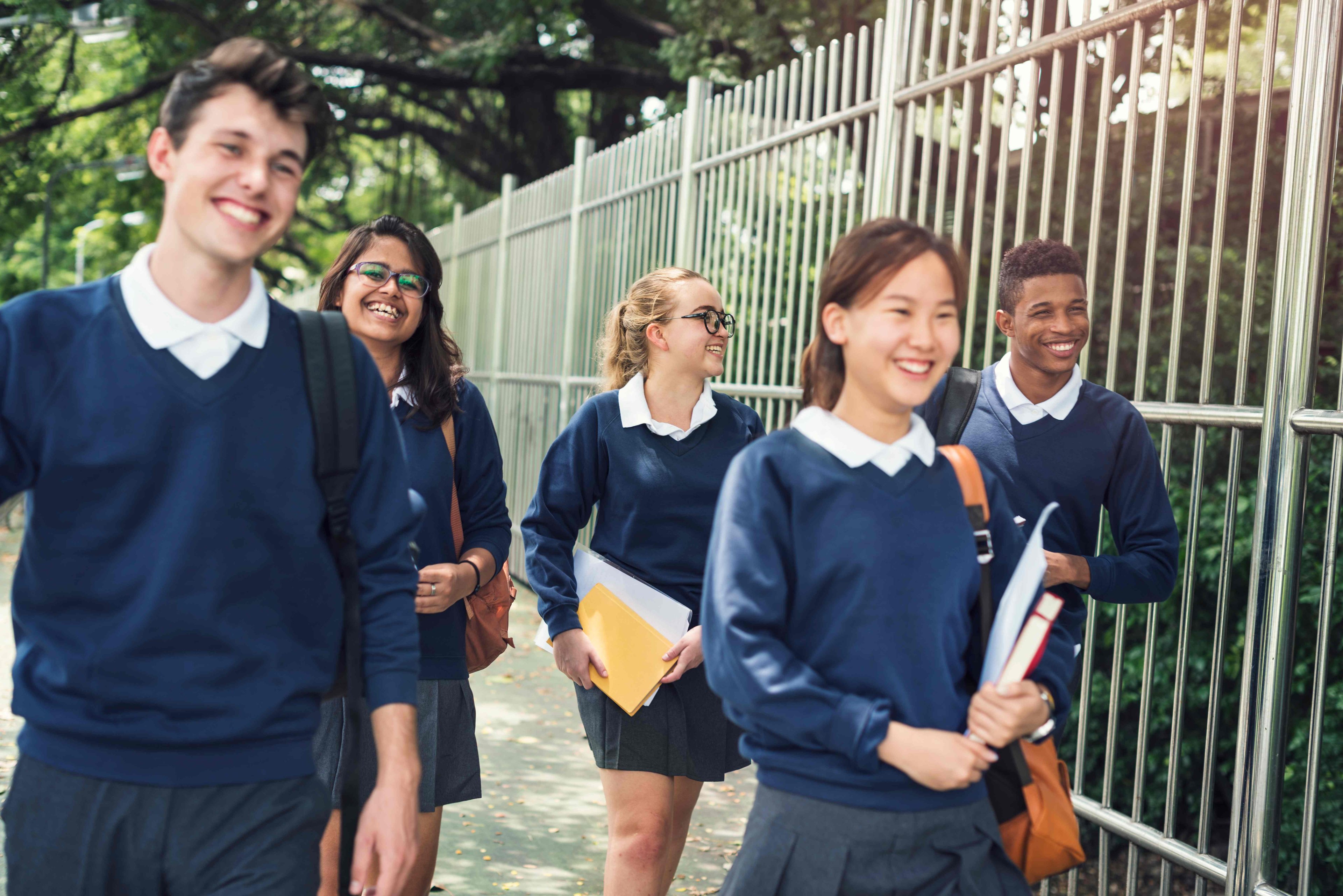 Group of teenagers in school uniform walking outdoors on a path, smiling and laughing