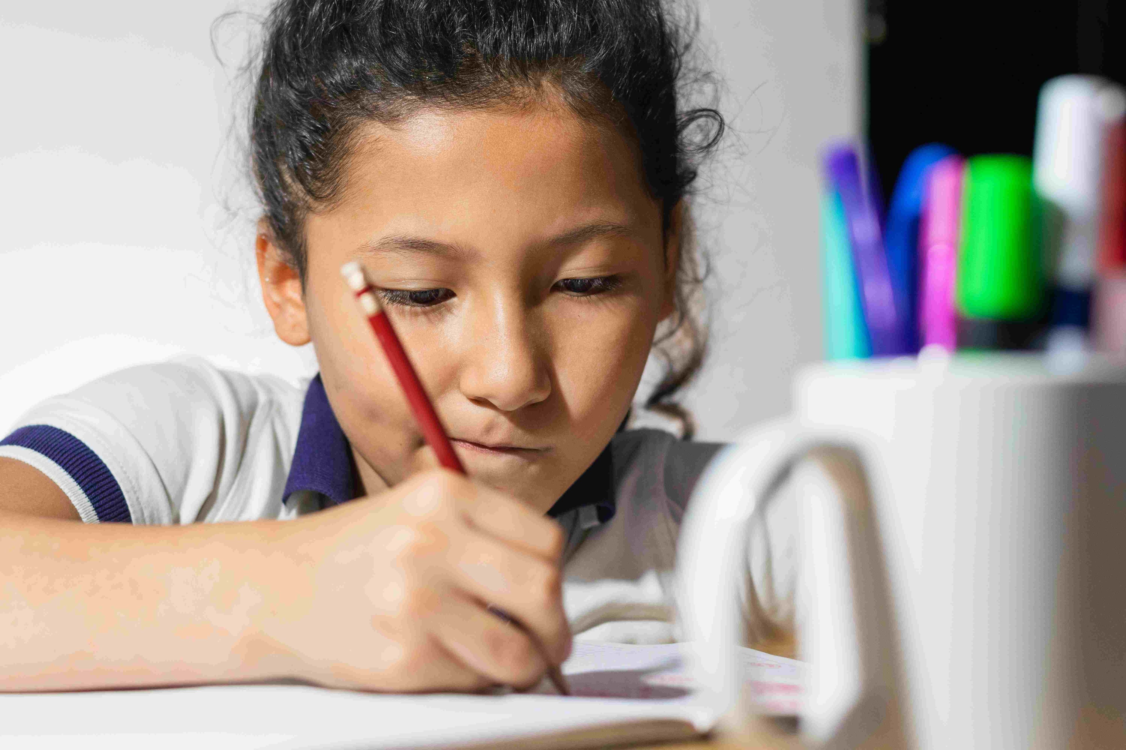 Child concentrating while writing in a notebook with a pencil