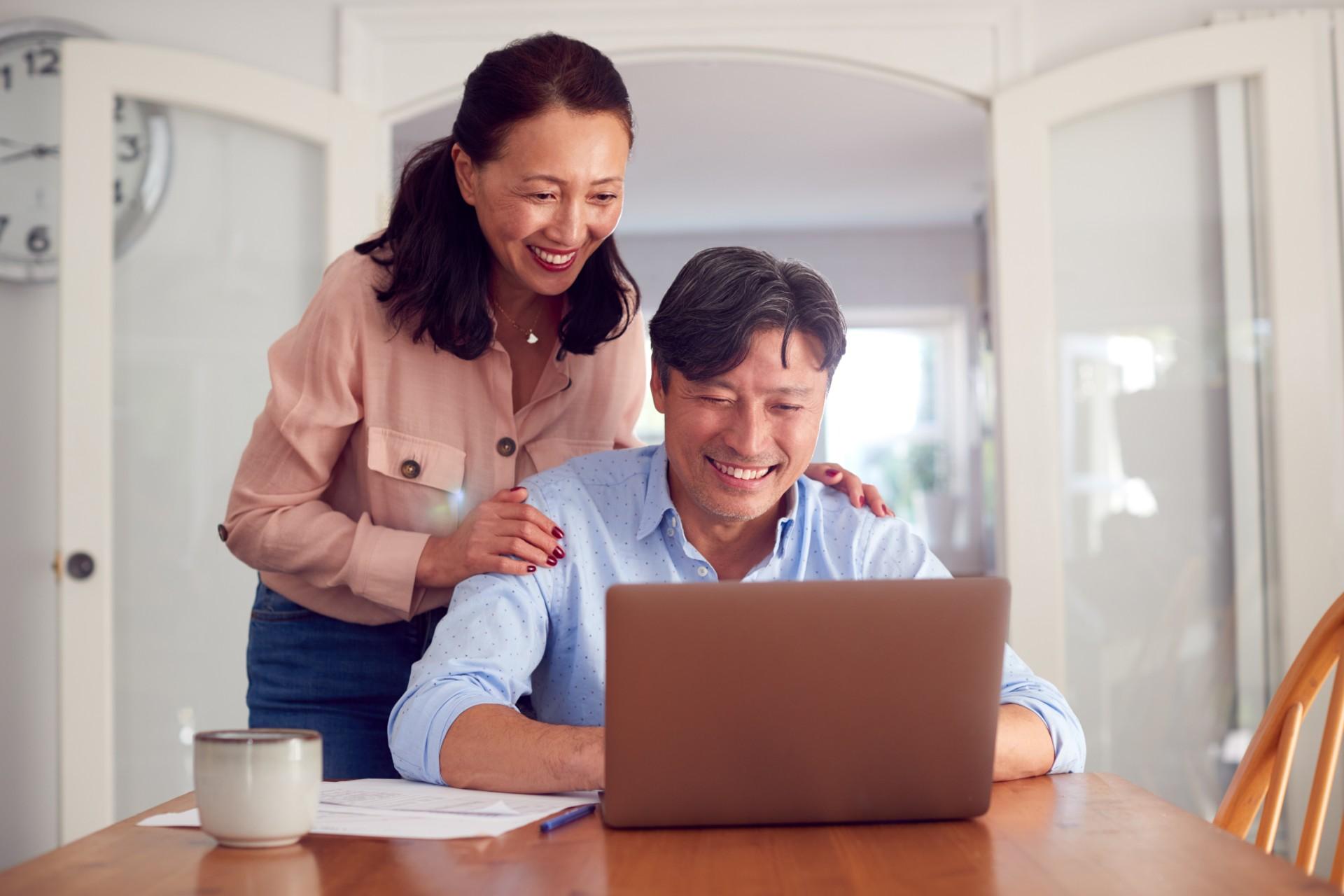 Middle-aged couple smiling while looking at a laptop on a dining room table