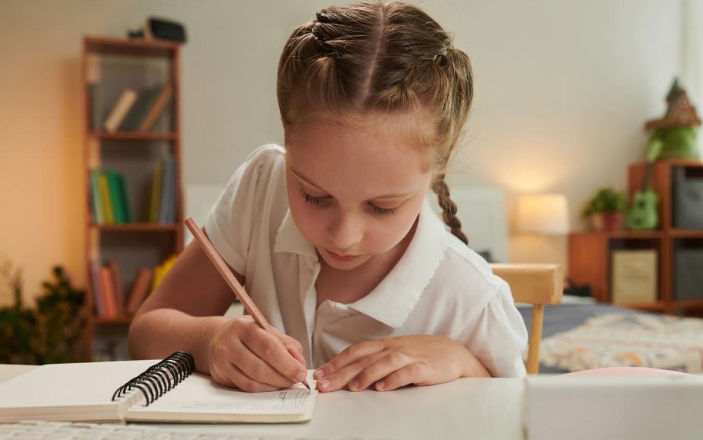 Young schoolgirl writing in a notebook at a table